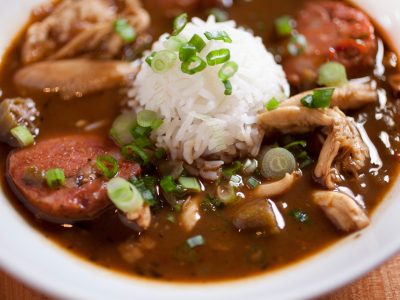 dark brown Cajun gumbo with chicken and sausage and scoop of white rice topped with green onion tops